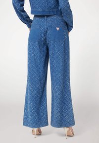 Blå denimbyxor med vida ben och ett mönstrat utseende, med två bakfickor och en liten logopatch. Kläderna har en lös och avslappnad passform.