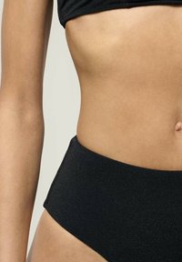 Pantaloni de bikini negri cu talie înaltă, fabricați dintr-un material texturat. Dispun de un tiv neted și un design fără cusături, cu detalii minime.