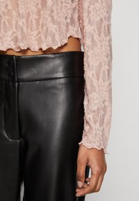 Ljusrosa spetsblus med lång ärm och vågig nederkant, kombinerad med högmidjade, släta svarta läderbyxor med knapppdetaljer.