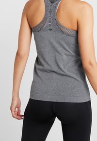 Grå, åtsittande atletisk linne med racerback-design, med en strukturerad meshöverkant och slät tyg från midjan och neråt. Svarta leggings.