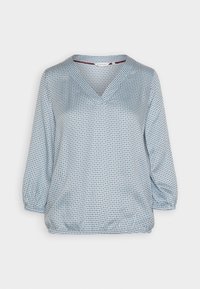 Blusa azul claro con escote en V, mangas tres cuartos y un patrón texturizado con pequeños puntos rojos y azul marino. Dobladillo elástico.
