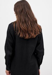 Black long-sleeve shirt made of linen with a relaxed fit, featuring a pointed collar and button cuffs, displayed from the back.