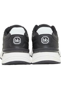 Crne atletske cipele s bijelim detaljima, koje imaju teksturirani gornji dio, podstavljeni ovratnik i grb na peti. Čvrsta gumena potplat.