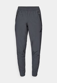Grå træningsbukser med elastisk talje, to lynlåslommer på siden og sorte detaljer. Fremstillet af strækbart, letvægtsmateriale.
