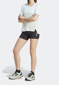 Vaaleansininen lyhythihainen urheilupaita, mustat kompressioshortsit sekä moniväriset maastokengät, joissa on teksturoitu pohja ja mustat nauhat.