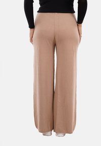 Pantaloni beige a gamba larga realizzati in tessuto morbido, con vita alta e texture liscia. Il design permette un movimento confortevole.