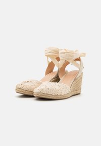 Beige gehaakte wedge espadrilles met een open teen, voorzien van een geweven juten zool en stofbanden die gekruist zijn en om de enkels zijn gestrikt.