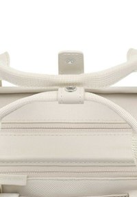 Gros plan sur la poignée d'un sac en tissu beige et la fermeture à bouton-pression avec des coutures visibles et des détails de texture.