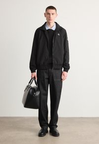 Crna zip-up jakna, crni pulover, svijetloplava košulja s ovratnikom, tamne traperice, crna torba i crne cipele. Minimalistički dizajn i teksture.