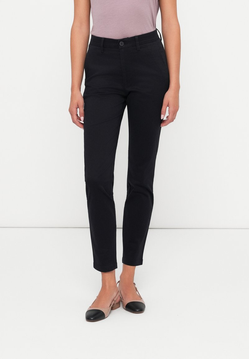 Zwarte broeken in een slim fit met een gladde textuur, voorzien van een knoopsluiting en opgerolde mouwen, gecombineerd met naakte en zwarte flats.