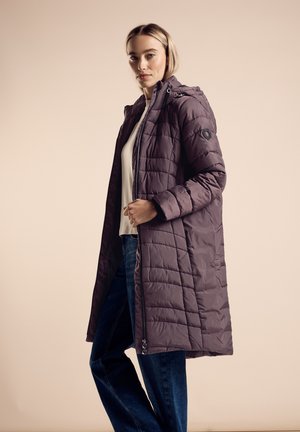 Padded long coat in dark purple with a zip front, hood, and side pockets. Textured quilted pattern. Paired with a white top and jeans.