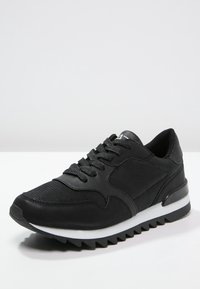 Černá sportovní bota s texturovaným koženým svrškem, šněrováním, silnou bílou mezipodešví a výraznou gumovou podrážkou.