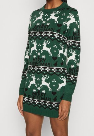 Zielona sukienka sweterkowa na Boże Narodzenie z białymi reniferami, płatkami śniegu, czarnymi sercami, drzewkami i napisem "Wesołych Świąt!", noszona przez osobę.