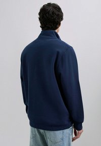Sudadera de polar de color azul marino con cuello alto y mangas largas, que presenta un ajuste relajado. Textura suave, diseño sencillo y sin patrones visibles.