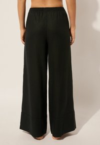 Pantalons larges noirs avec une taille élastique, présentant une texture lisse et sans motifs visibles. Les finitions des ourlets sont soigneusement confectionnées.