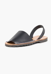 Sandalo slingback in pelle nera con punta aperta, design curvo e cuciture tonalità su una suola marrone. Suola texturizzata per un'ottima aderenza.