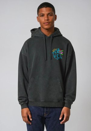 Zwarte hoodie van zacht materiaal, met een voorzak en een kleurrafische haai op de borst. Ontspannen pasvorm en geribbelde manchetten.