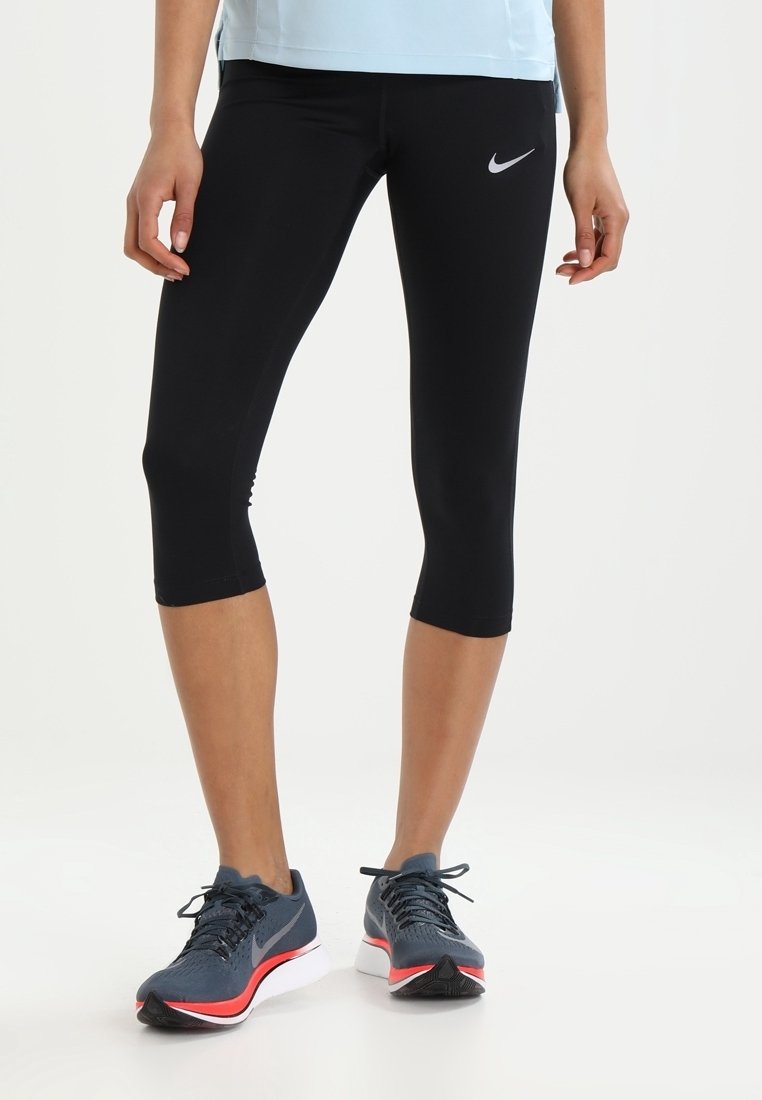 Legs wearing black Nike cropped leggings and gray Nike running shoes with red and white soles, standing on a white background.