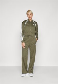 Ελιόχρωμο αθλητικό σετ με λευκές ρίγες στα μανίκια και στα παντελόνια, ζακέτα με φερμουάρ και παντελόνια με κορδόνι στη μέση. Λείος ύφασμα, αθλητική εφαρμογή.