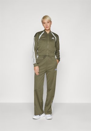 Tuta verde oliva con strisce bianche sulle maniche e sui pantaloni, giacca con zip e pantaloni con coulisse in vita. Tessuto morbido, vestibilità atletica.