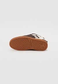 Braune Sneaker mit einem kontrastierenden weißen Sternlogo, Gummiaußensohle mit texturiertem Grip und einer abgerundeten Zehenform. Das Obermaterial hat eine weiche Stoffoberfläche.