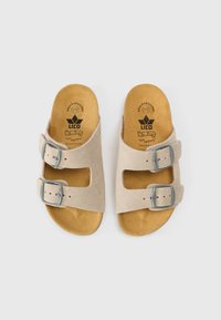 Bézs nyersbőr szandál két állítható szürke csattal, formázott barna párnázott talppal és a márka logójával a talpbetéten.