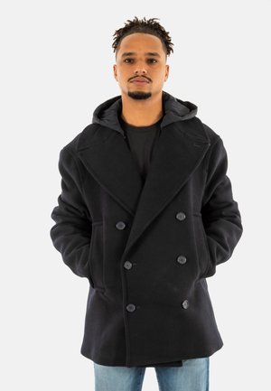 Cappotto nero doppiopetto con un design aderente, ampi revers e cappuccio. Presenta chiusure a bottoni e tasche laterali, indossato sopra una camicia nera.