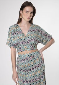 Top avvolgente a maniche corte con scollatura a V in tessuto fantasia che presenta un motivo a diamante blu tealc, rosa, giallo e nero, abbinato a una gonna coordinata.