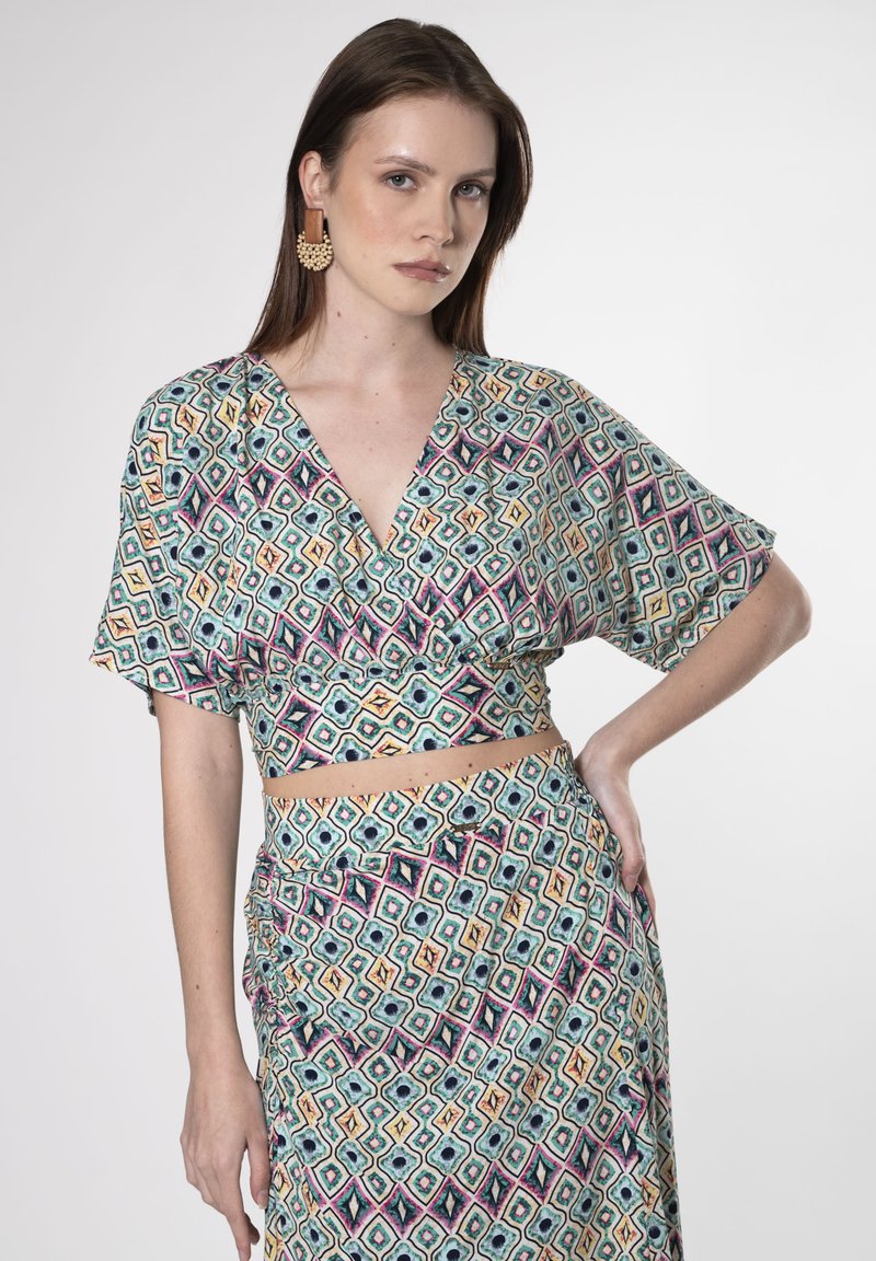 Top de manga corta, con escote en V y cierre envolvente, en tela de estampado que presenta un diseño de diamantes en tonos verde azulado, rosa, amarillo y negro, acompañado de una falda a juego.