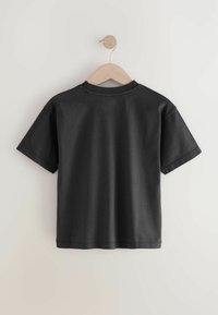 Sort bomulds t-shirt med korte ærmer, rund hals og en afslappet pasform, hængende på en træholder mod en lys baggrund.