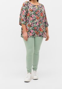 Blusa floral con fondo negro, que presenta patrones vibrantes en rosa, rojo y verde, combinada con jeans skinny verde claro y zapatillas blancas.