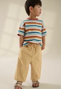 Gestreepte t-shirt met korte mouwen in rood, blauw en geel; beige joggingbroek met koord; en bruine sandalen met gespen.