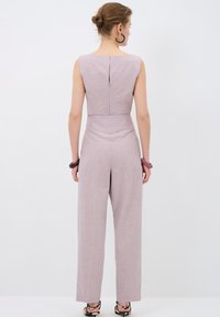 Tuta senza maniche rosa chiaro con un corpetto aderente e pantaloni larghi e ampi. Tessuto testurizzato con una chiusura zip discreta sul retro.