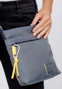 Borsa a tracolla texture blu navy con motivo geometrico bianco, accenti gialli, hardware argentato e tracolla regolabile. Tasca frontale con zip.