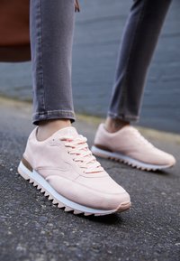 Chaussures de sport rose clair avec tiges en nylon texturé, semelles blanches et semelle à motif zigzag. Dotées de lacets avant et d'une silhouette profilée basse.