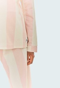 Lekka, miękka odzież wypoczynkowa z bawełny w pastelowe różowe i kremowe paski, o prostym kroju i widocznym znaczku marki na rękawie.