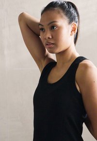 Čierny bezrukávový športový top so priliehavým strihom, okrúhlym výstrihom a hladkou textúrou. Pozadie je v svetlej neutrálnej farbe.