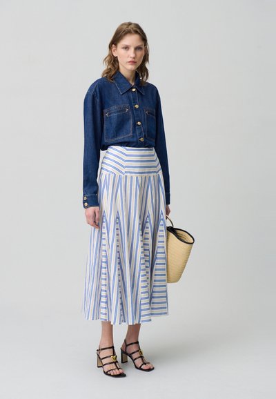 Camisa de mezclilla recortada con botones dorados, falda maxi de rayas plisada en azul y blanco, y sandalias negras con tiras. Incluye una bolsa de mimbre.