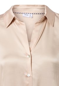 Beige satin blouse with a classic collar, featuring front button closure and smooth texture. Tag visible with brand name and size.