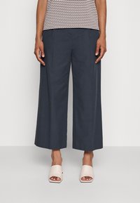 Szerokie, ciemnoniebieskie spodnie wykonane z gładkiego materiału, z dopasowanym krojem i pliskami. Połączone z jasnoróżowymi klapkami z odsłoniętą palcami.