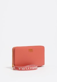 Billetera de cuero coral con logo dorado, cierre de cremallera y correa de muñeca de tela con un patrón repetido del nombre de la marca. Textura suave y forma rectangular.