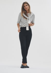 Fekete leggings fehér és tengerészkék csíkos felsővel párosítva, könnyű sállal kiegészítve. A ruházat laza szabású és sima textúrájú.