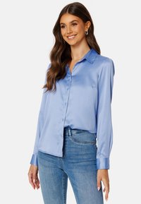 Blusa di satin blu chiaro con colletto classico, maniche lunghe e chiusura a bottoni. Presenta una texture liscia e una vestibilità rilassata.