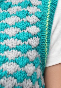 Dzianinowa kamizelka z naprzemiennymi wzorami serc w turkusowym i szarym kolorze, o fakturowanym wykończeniu. Wykończona jasnym żółtym brzegiem.