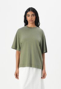 Olijfgroen oversized t-shirt van zachte katoen, met een ronde halslijn en korte mouwen, getoond met een witte kanten rok.
