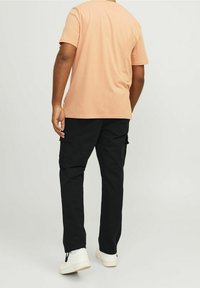 Brzoskwiniowy bawełniany t-shirt z okrągłym dekoltem i krótkimi rękawami, w połączeniu z czarnymi spodniami bojówkami z bocznymi kieszeniami i zwężanymi mankietami, noszony z białymi trampkami.