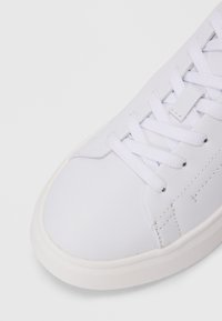Sneaker alb cu o parte superioară din piele netedă, vârf rotund și talpă din cauciuc plat. Dispune de șireturi albe și detalii de cusătură minime.