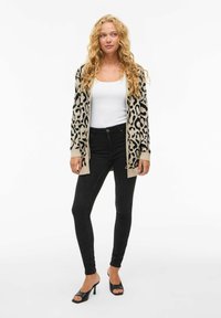 Cardigan de estampado de leopardo en beige y negro, con apertura frontal y puños acanalados, combinado con jeans negros ajustados y sandalias negras de tacón.