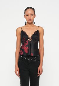 Top in camicia floreale nera e rossa con pizzo, scollatura a V profonda e chiusura con cravatta davanti, abbinato a jeans neri a vita alta con borchie.