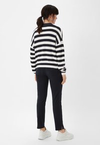 Gestreifter Strickpullover in Marineblau und Weiß, mit lockerer Passform, langen Ärmeln und gerippten Bündchen, kombiniert mit dunklen Hosen mit Seitenschlitzen.
